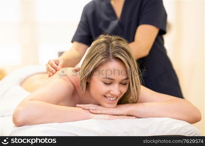 Young woman lying on a stretcher receiving a back massage in a spa center.. Woman lying on a stretcher receiving a back massage.