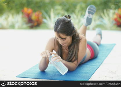 Young woman lying on an exercise mat holding a water bottle