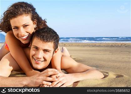 Young woman lying on back of man on beach, portrait, ground view