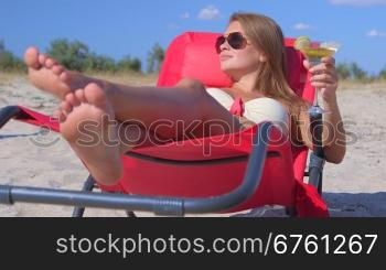 Young woman lying on beach lounger with cocktail enjoying summer vacation