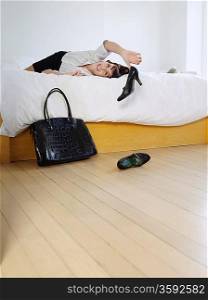 Young woman lying on bed throwing high heeled shoes on floor