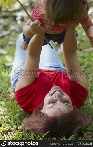 Young woman lying on grass and picking up her daughter
