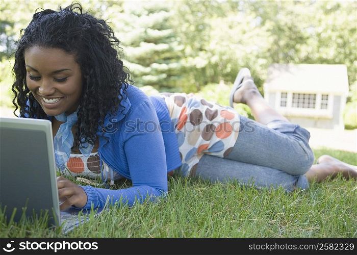 Young woman lying on grass and using a laptop