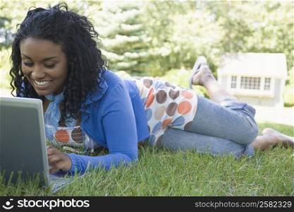 Young woman lying on grass and using a laptop