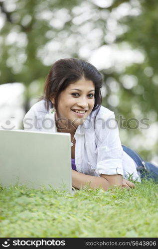 Young woman lying on grass in lawn and using laptop