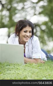 Young woman lying on grass in lawn and using laptop