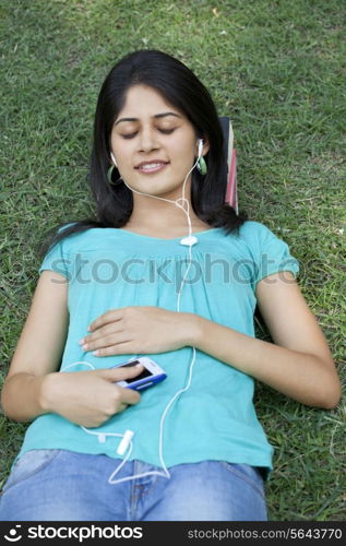Young woman lying on grass listening to mp3 player