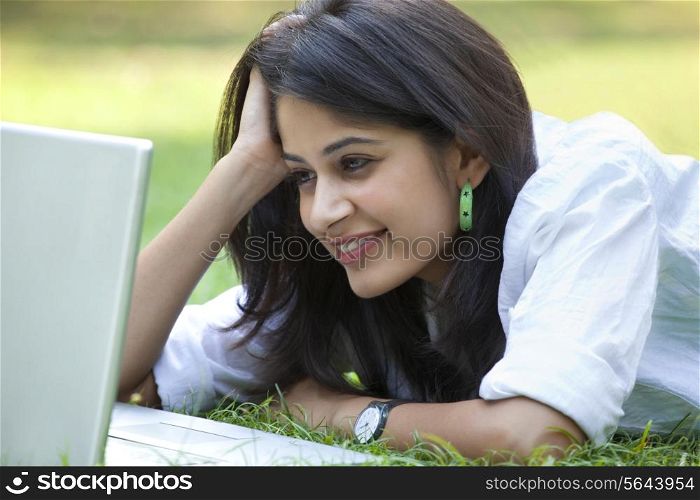 Young woman lying on grass using laptop