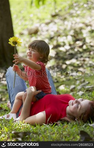 Young woman lying on grass with her daughter sitting on her stomach