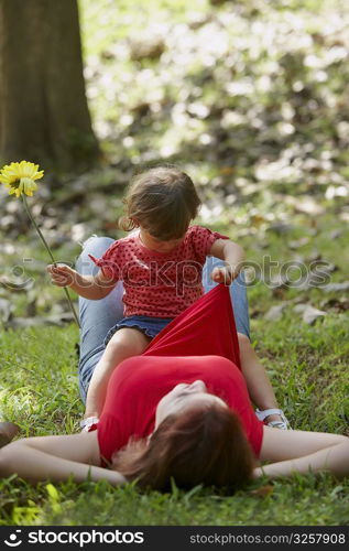 Young woman lying on grass with her daughter sitting on her stomach