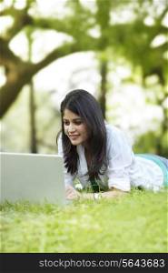 Young woman lying on green grass and using laptop