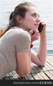 Young woman lying on pier chatting on smartphone, Lake Mergozzo, Verbania, Piemonte, Italy