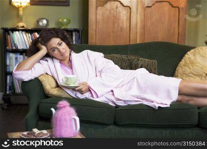 Young woman lying on sofa at home drinking tea