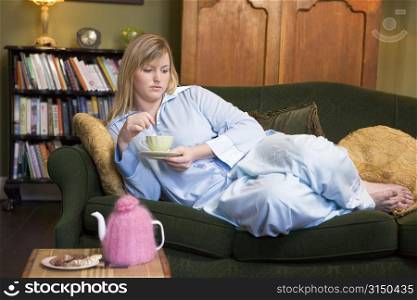 Young woman lying on sofa at home drinking tea