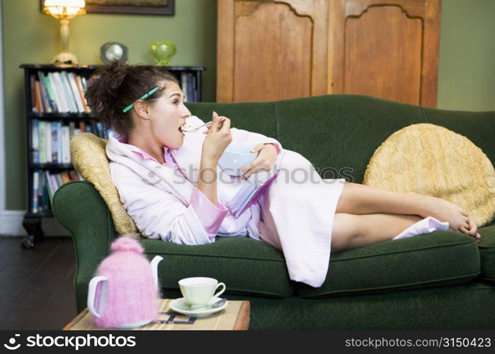 Young woman lying on sofa at home eating a sweet treat