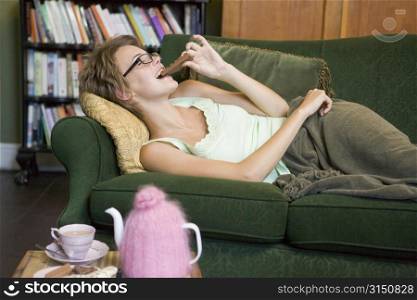 Young woman lying on sofa at home eating chocolate