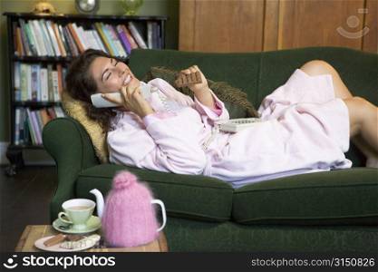 Young woman lying on sofa at home eating chocolate and talking on telephone