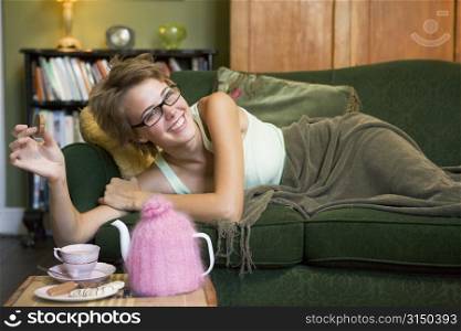 Young woman lying on sofa at home eating cookies and drinking tea