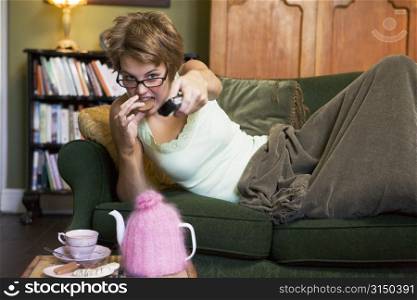 Young woman lying on sofa at home eating cookies and watching television