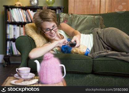 Young woman lying on sofa at home eating potato chips and watching television