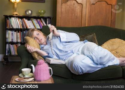 Young woman lying on sofa at home holding telephone