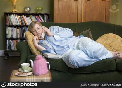 Young woman lying on sofa at home talking on telephone