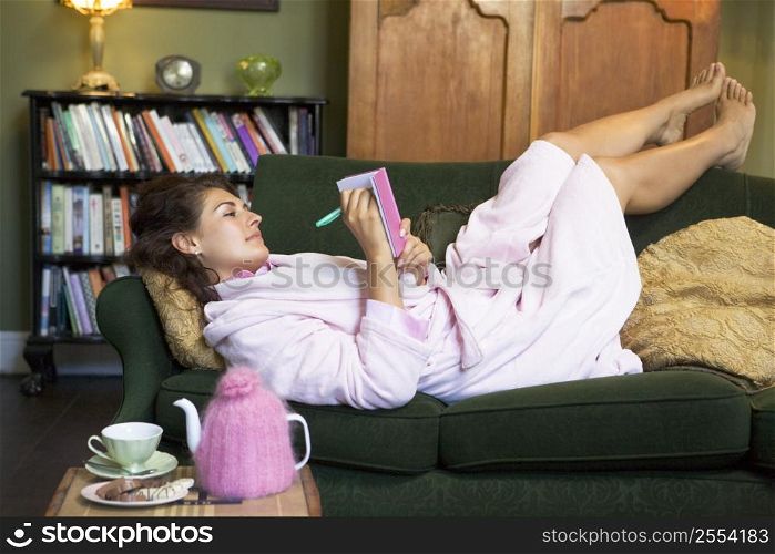 Young woman lying on sofa at home writing in her diary