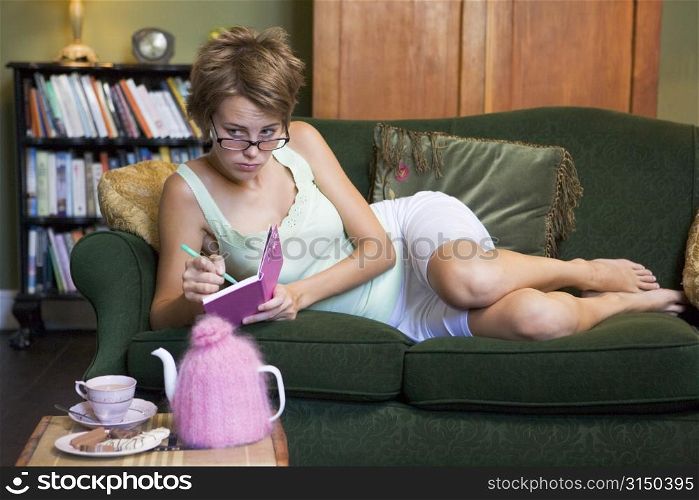 Young woman lying on sofa at home writing in her diary