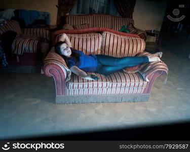 Young woman lying on sofa at night and watching television