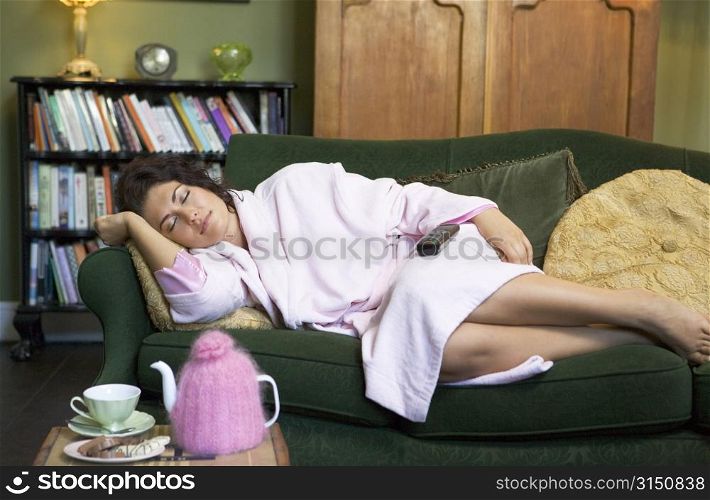 Young woman lying on sofa falling asleep while watching television
