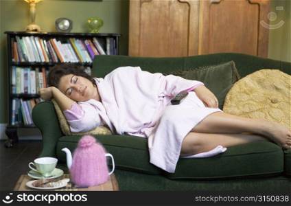 Young woman lying on sofa falling asleep while watching television