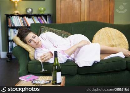 Young woman lying on sofa smoking and drinking wine
