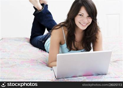 Young woman lying on the bed and using a laptop