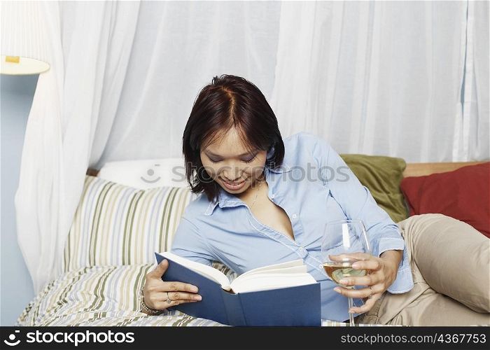 Young woman lying on the bed reading a book