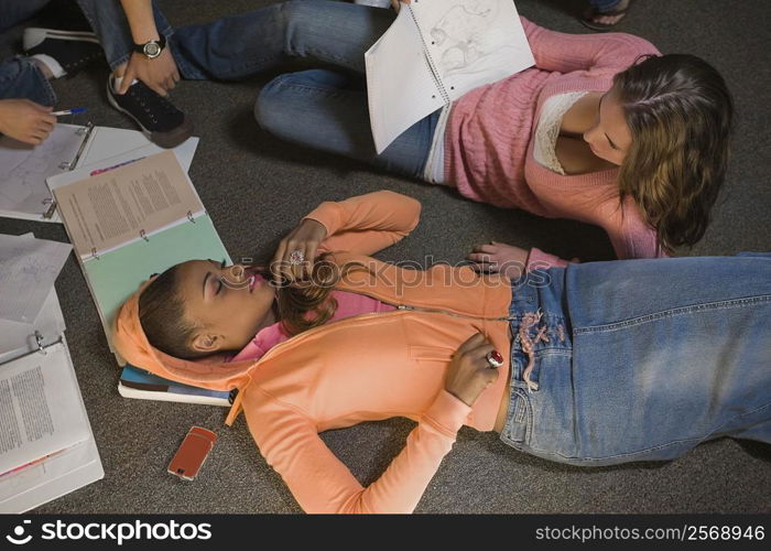 Young woman lying on the floor and another young woman holding a book beside her