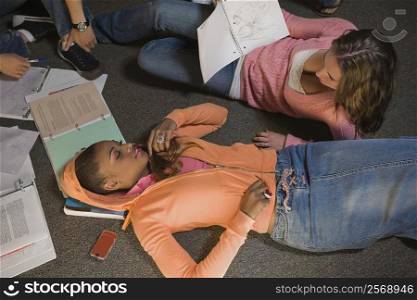Young woman lying on the floor and another young woman holding a book beside her
