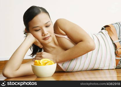 Young woman lying on the floor with a bowl of orange slices in front of her
