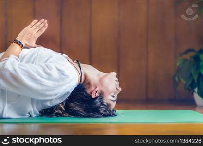 Young woman lying on the turquoise yoga mat in fish pose with hands in prayer position.