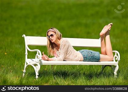 Young woman lying on white bench on sunny day; shallow DOF