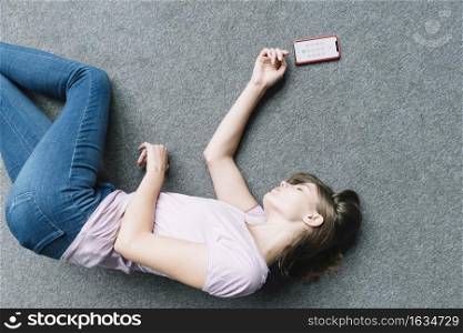young woman lying unconsciously carpet near smart phone