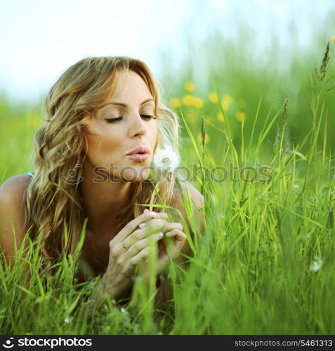 Young woman makes a wish blowing on dandelion