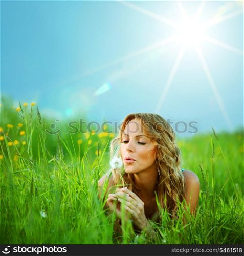 Young woman makes a wish blowing on dandelion