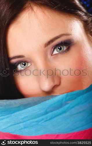 Young woman makeup on eyes hiden her face with multicolored shawl blue background