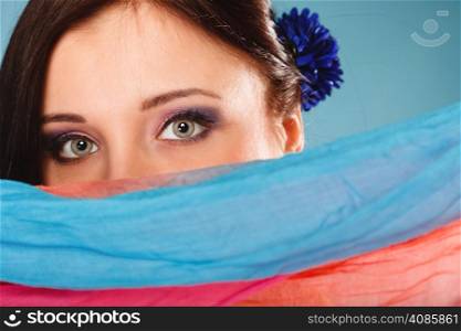 Young woman makeup on eyes hiden her face with multicolored shawl blue background