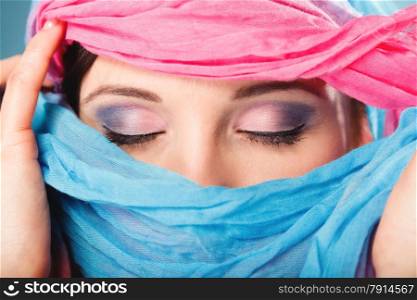 Young woman makeup on eyes hiden her face with multicolored shawl blue background