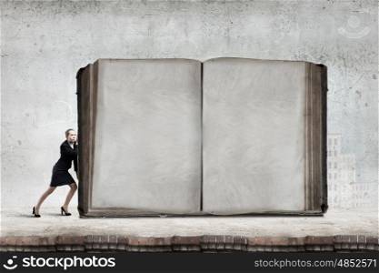 Young woman making effort to push huge old book. Books and reading