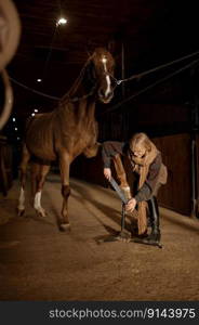 Young woman making horses hoof manicure, filing and shaping horseshoe. Stallion grooming and cleaning before riding. Young woman making horses hoof manicure, filing and shaping horseshoe