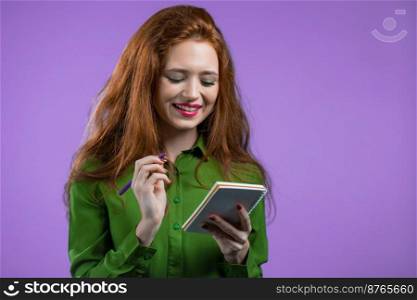 Young woman making notes in planner, lady holding pen. She writes future plans and to-do list in notebook for week or month. Keeping personal diary on purple studio background. High quality photo. Young woman making notes in planner, lady holding pen. She writes future plans and to-do list in notebook for week or month. Keeping personal diary on purple studio background.