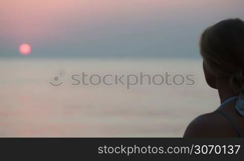 Young woman making photo of sunset over sea using touch pad. At first focus on woman with pad, then on sunset and man swimming in the distance