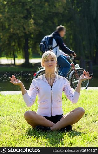 young woman making yoga pose in the park near the river
